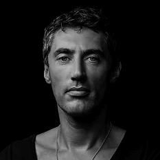 Black and white portrait of Edward Van Vliet against black, showing textured hair, defined features, and a silver chain necklace.