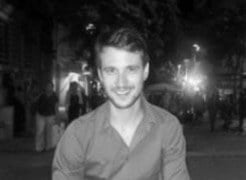 Black and white portrait of Ivan Paradinovic, smiling, wearing a collared shirt, blurred city street background with bokeh lights.