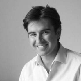Black and white portrait of Lorenzo Gecchelin, a man with dark wavy hair, wearing a white button-down shirt, against a neutral gray background.