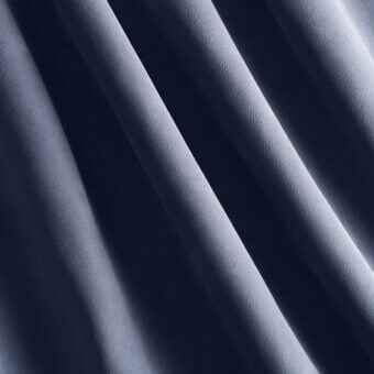 Gray draped fabric with parallel folds creates a diagonal pattern, showcasing a smooth, matte texture and subtle woven grain under soft lighting.
