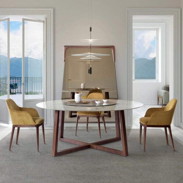 Dining room with marble table, walnut base, yellow armchairs, tiered pendant light, mirror, and lake view.