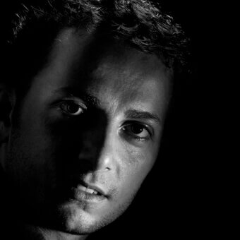 Black and white portrait of Stefano Traverso, studio shot, high contrast lighting, dark curly hair, serious expression, direct gaze.