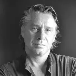 Black and white portrait of Valerio Bottin, a man with light hair and beard, wearing a dark collared shirt, against a solid gray background.