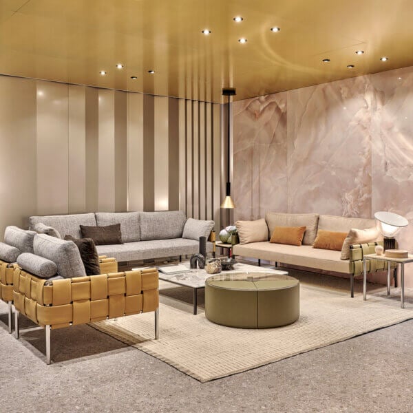 Living room with gray & beige sofas, leather armchair, olive & glass tables, marble wall paneling, gold ceiling, terrazzo floor.