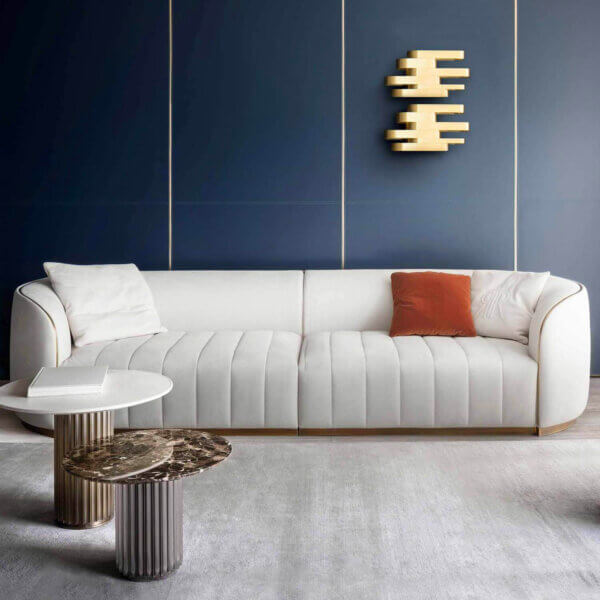 Rugiano Pierre sofa, ivory channel-tufted upholstery, modular design with gold metal base, set in a navy blue room with gold accents.