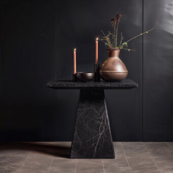 Black marble side table with square top and pyramidal base, styled with brown bowl, rose candles, and vase with dried floral arrangement.