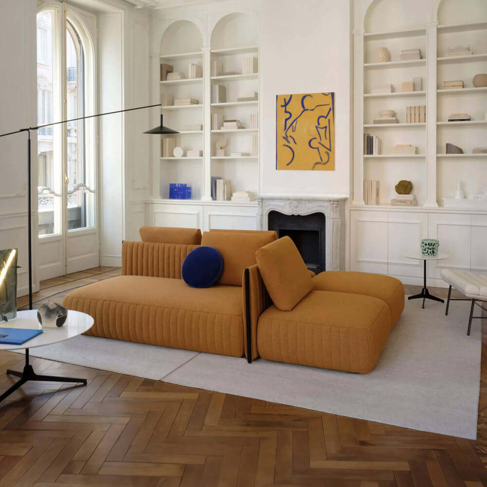 Modular sofa, mustard yellow fabric, pleated chaise lounge, with navy and orange cushions, centered in a minimalist living room interior.