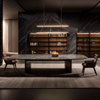 Oval marble dining table with dark walnut base, flanked by leather chairs, against dark veined marble walls and wood bookshelves.