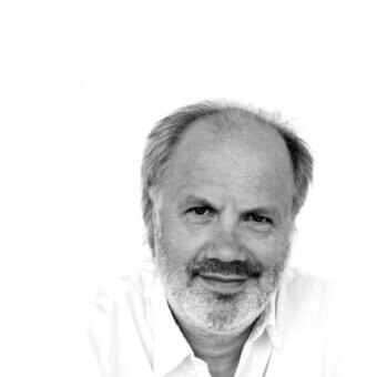 Black and white portrait of Aldo Cibic, gray hair and beard, light collared shirt, calm expression, close-up head and shoulders shot.