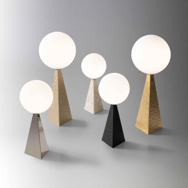 Stillux lamps with opaque white globes on textured gold, silver, black, and marble pyramid bases, studio lighting.