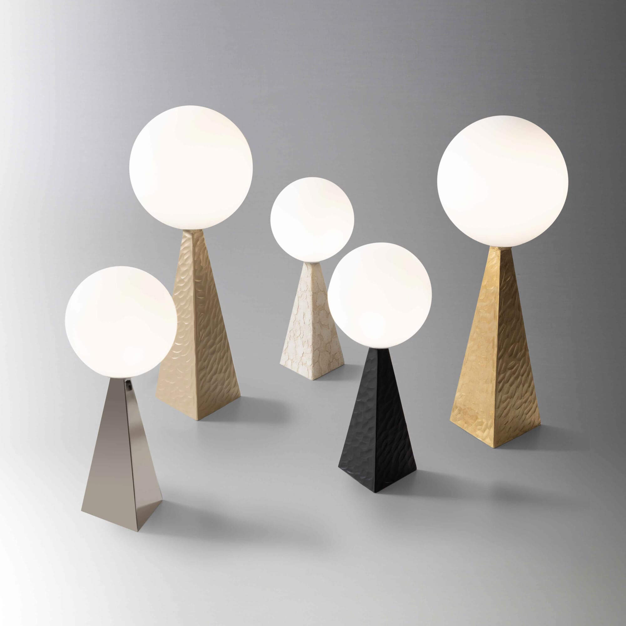 Stillux lamps with opaque white globes on textured gold, silver, black, and marble pyramid bases, studio lighting.