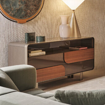 Turri Soul dresser, dark gray metal frame, walnut veneer drawers, glass top with books and green marble objects, beige sofa and lamp.
