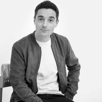 Modern molded plastic chair with curved back and light gray cylindrical legs, featuring Federico Agni in a gray bomber jacket.