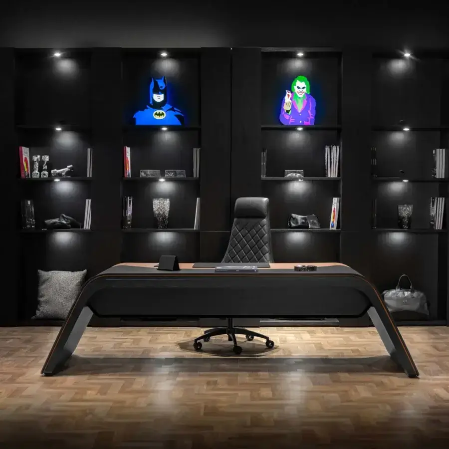 Rectangular desk with black glossy surface, light wood angular base, silver handle, and bat figurine, paired with black leather executive chair.
