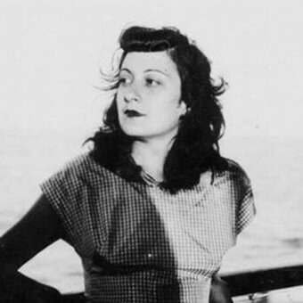 Lina Bo Bardi portrait, black and white photograph, checkered blouse, wavy dark hair, contemplative gaze, blurred outdoor background.