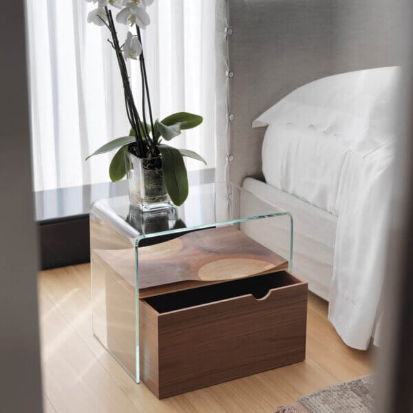 Cassoni Horm Bifronte bedside table, dark wood base, rectangular shape with glass top displaying white orchids in a vase, modern bedroom setting.