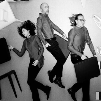 Three people in dark clothing levitate above gray floor with scattered modern chairs, studiocharlie, dynamic poses, briefcases held.