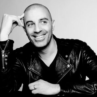 Bald man Dror in black leather biker jacket with quilted shoulders, silver zippers, and V-neck shirt against a white background.