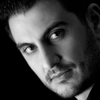 Black and white portrait of Salvatore Indriolo, close-up with dark hair and beard, focused gaze, dramatic lighting, monochrome aesthetic.
