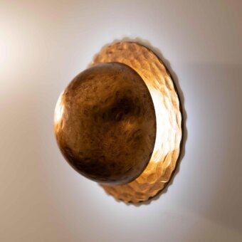 Distinguished Stillux Orbis wall lamp with a hammered metal surface in golden-brown, emitting ambient light from a spherical cover