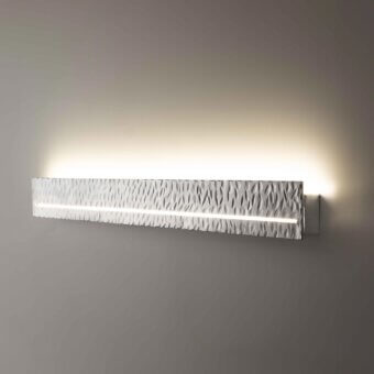 Architectural Stillux Random wall lamp with a horizontally oriented hammered metal frame emitting a soft glow in light gray