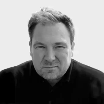 Black and white portrait of Antti Kotilainen, a man with gray hair and beard, wearing a dark shirt against a white background.