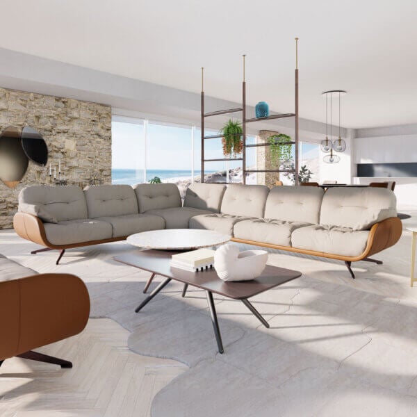 Beige modular sectional sofa with brown leather accents, marble coffee table, brass shelving, stone wall, coastal view.