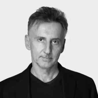 Black and white portrait of Leonardo Rossano, a man with short gray hair wearing a black blazer and t-shirt, neutral expression.