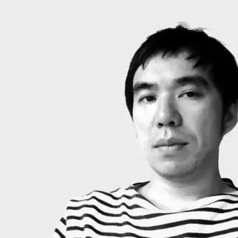 Takashi Shinozaki portrait, grayscale photograph, striped shirt, neutral expression, close-up, light gray background, minimal shadows.