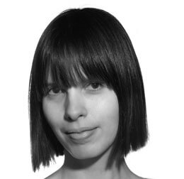 Grayscale portrait of a woman with a short bob haircut and blunt bangs, neutral expression, smooth skin, and stark white background.