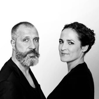 Black and white portrait of a man with beard and woman in turtleneck, facing forward against white backdrop, featuring “harry&camila”.