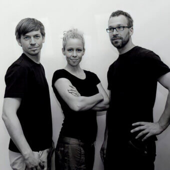 Black and white studio portrait of three people with minimalist styling, featuring neutral expressions and casual clothing, with “puldeskern” text.
