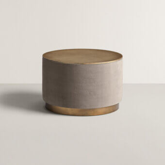 Cylindrical coffee table, taupe velvet upholstery, brushed brass top and base, minimalist design, textural contrast, modern style.