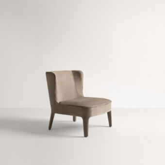 Frag lounge chair, taupe suede upholstery, curved high back, tapered legs, minimalist design, contemporary seating, diffused lighting.