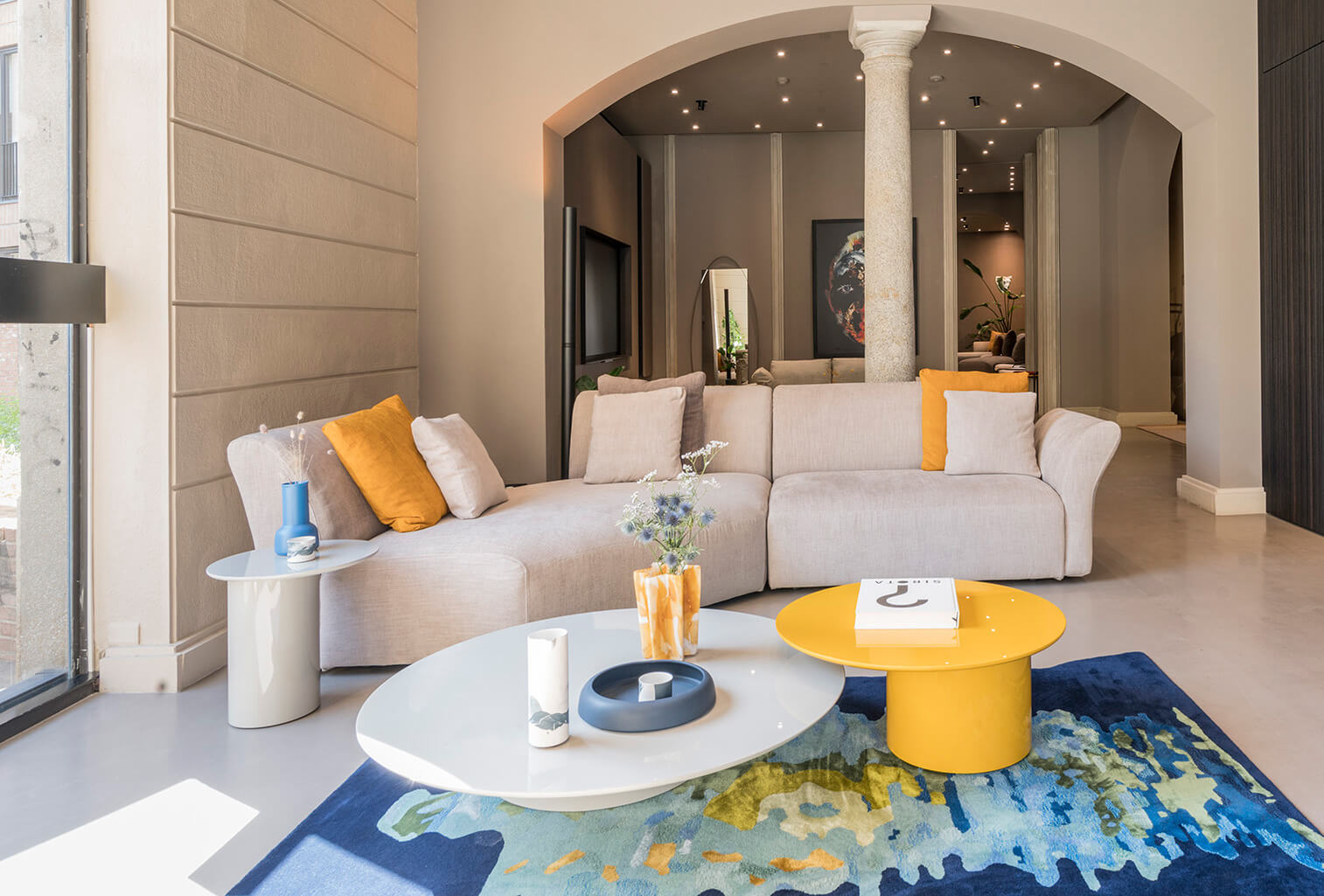 Modular sofa, light gray fabric, rounded cushions, with circular coffee table, blue and yellow, on abstract rug, blue, green hues.