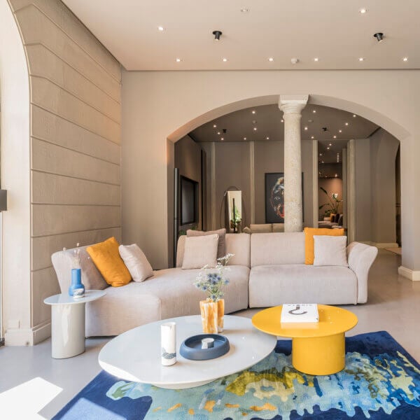 Light gray modular sectional sofa with orange pillows, yellow coffee table, and abstract rug in a modern living room setting.