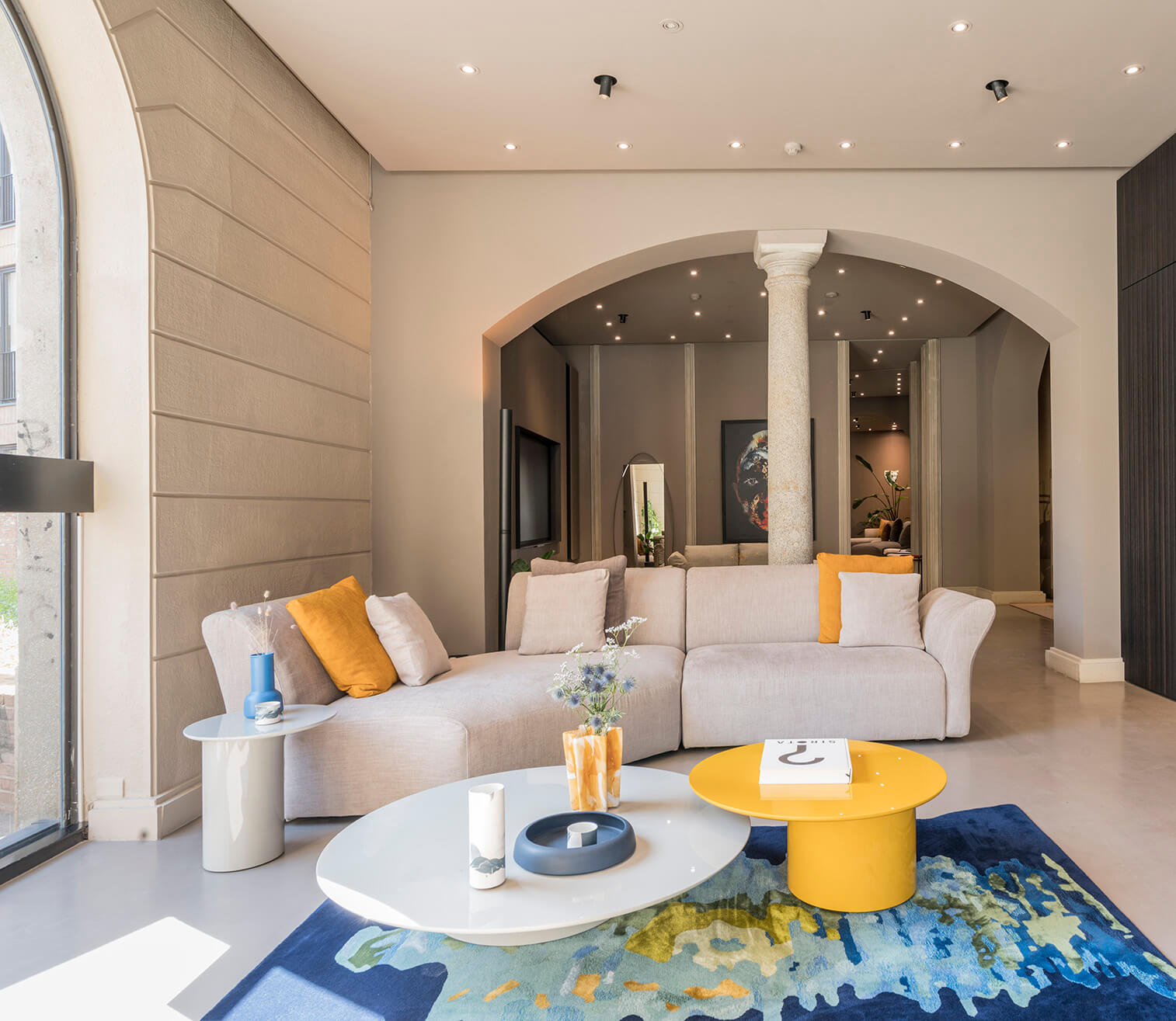 Light gray modular sectional sofa with orange pillows, yellow coffee table, and abstract rug in a modern living room setting.