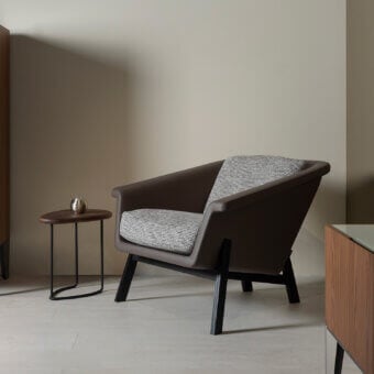 Distinguished Horm Sienna lounge chair with enveloping form upholstered in brown material and light grey textile cushions with dark wood legs