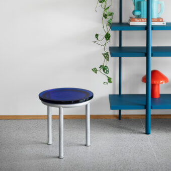 Miniforms Zigo side table, deep blue glossy surface, with white tapered cylindrical legs, styled with books and plants.