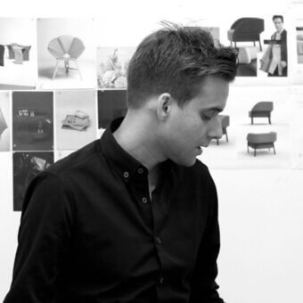 Studio view of man near wall displaying furniture design prints, including chairs and a radiating table, in a minimalist setting.