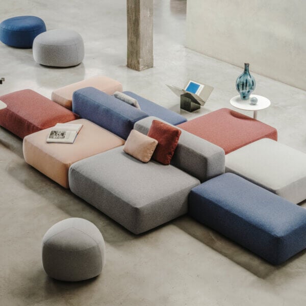Modular sofa system, rose, blue, gray upholstery, square cushions, circular arrangement, silver leg side tables, concrete floor.