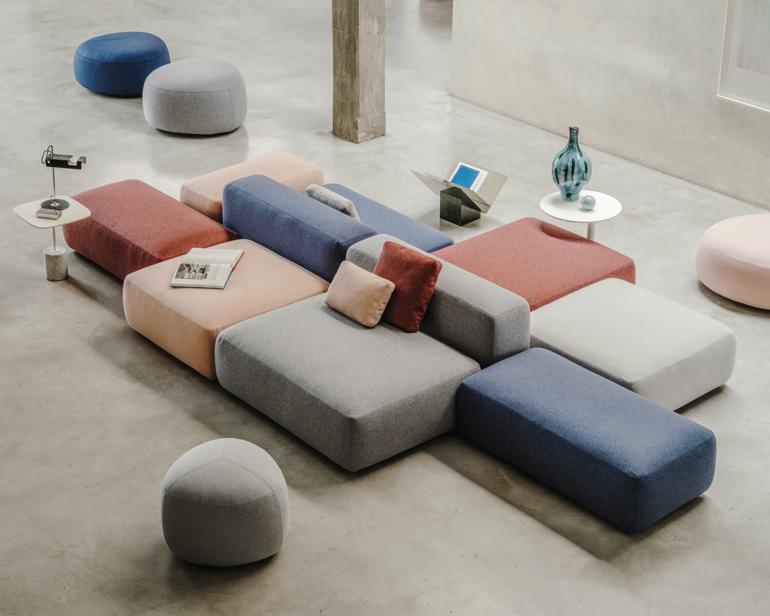 Modular sofa system, rose, blue, gray upholstery, square cushions, circular arrangement, silver leg side tables, concrete floor.