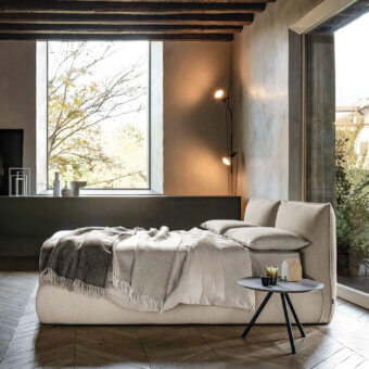 Bolzan Letti Venus bed, beige upholstered headboard, rectangular shape, with grey marble side table, linen bedding, and grey plaster walls.