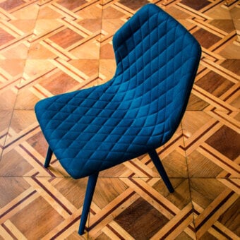Superior Bross Ava chair with dark blue fully upholstered shell and quilted inner back, built with lacquered metal legs