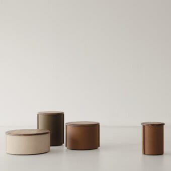 Cierre 1972 side tables, wood and leather, staggered cylindrical arrangement with varying heights and brown, beige, green tones.