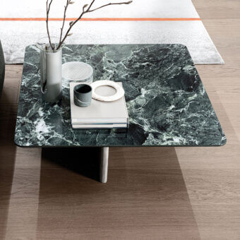 Wings coffee table, green marble top with white veining, single gray metal leg, styled with vase, dish, books on wood floor.