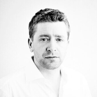 Black and white portrait of Constantin Wortmann, short dark hair, light shirt, neutral expression, plain light gray background, soft lighting.
