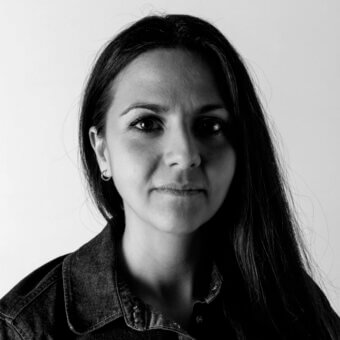 Francesca Smiraglia portrait, black and white photograph, denim jacket, neutral expression, simple hoop earring, white background.