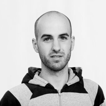 Man Tobias Juretzek, gray hooded sweatshirt, shaved head, neutral expression, white background, diffused lighting, portrait.