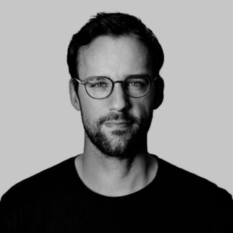 Black and white portrait of Robert Dabi with short dark hair, salt-and-pepper beard, and round glasses, wearing a black t-shirt.